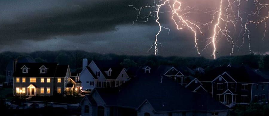 Lightning striking over a suburban neighbourhood at night, one house still lit